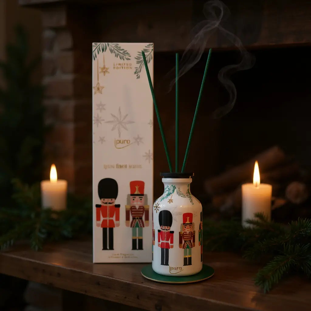 Limited edition Finest Season diffuser met kerstig ontwerp; flessenbasis met nutcracker-figuren en groene rieten stokjes, naast doos en brandende kaarsen.