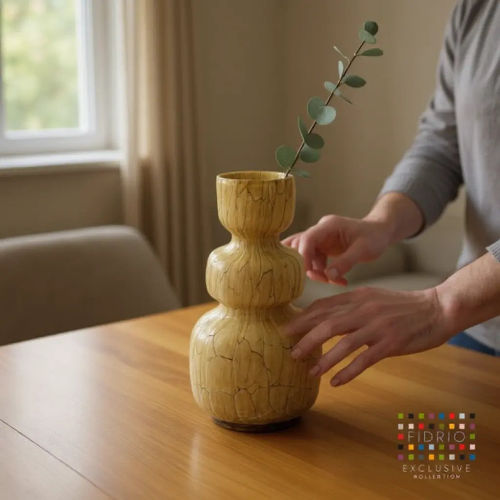 Houten vaas met krullende, drie-verdikking en tak van eucalyptus op een houten tafel; vaas heeft natuurlijke nerven, FIDRIO logo op hoek.